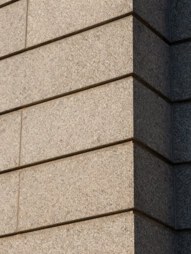 Abstract architectural close-up of a granite building facade in Cheyenne, sharp clean stone lines, subdued morning light.