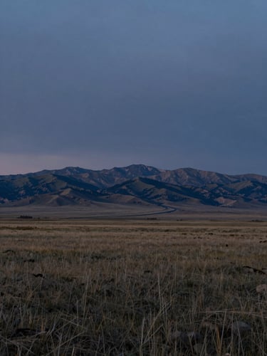 Expansive wide shot of the Wyoming plains under a low-light, moody twilight sky, distant mountains, grounded and quiet.