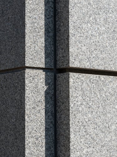 Abstract architectural close-up of heavy granite blocks meeting with absolute precision, sharp shadow lines, cool natural light.