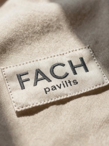 Extreme close-up of a heavy linen garment label stitched with minimalist charcoal typography, soft natural window light casting gentle shadows on champagne beige fabric.