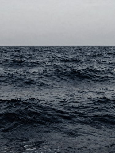 Slow-motion desaturated ocean waves, deep navy and muted slate tones, minimalist composition, 35mm film photography.