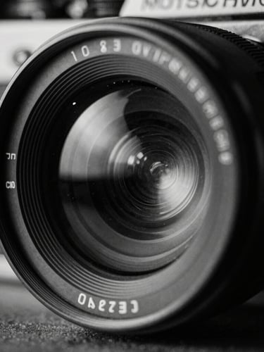 Extreme close-up of a high-contrast 35mm film camera lens reflecting dramatic studio lights, stark shadows, cool-toned monochrome, raw cinematic texture.