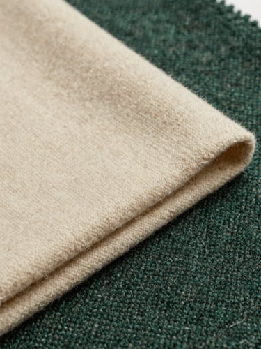 Close-up of premium folded wool and tweed fabrics in warm cream and deep green tones, soft natural gallery lighting, editorial fashion photography