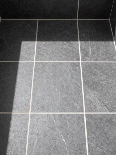 Sharp architectural photography of a modern bathroom floor, straight-on overhead view of perfectly aligned charcoal porcelain tiles with crisp white grout lines, bright natural daylight, high-contrast, 35mm