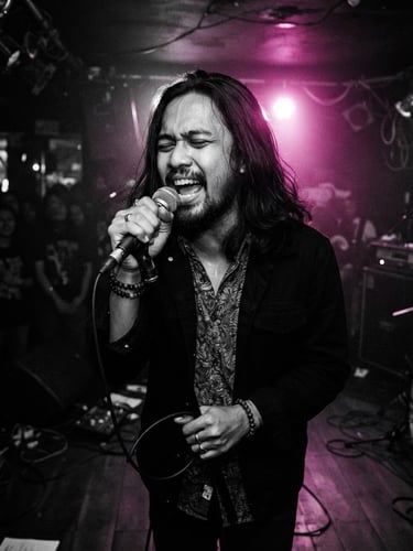 High-contrast black and white photo of a passionate Indonesian indie musician singing on a dark stage, dramatic magenta backlighting, moody atmosphere, 35mm lens
