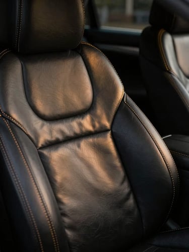Ultra close-up of precision hand-stitched leather seat covers inside a luxury vehicle, gold contrast stitching on black leather, dramatic low-key studio lighting, sharp metallic reflections, 35mm lens
