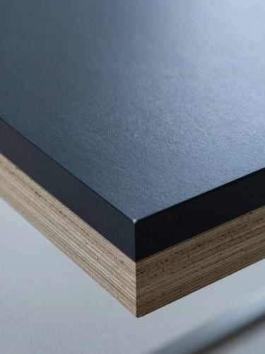 Macro close-up of dark phenolic film faced plywood, showcasing the glossy, uniform surface and sealed edges under clean technical lighting.