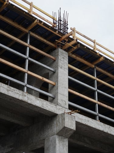Low-angle heroic shot of active concrete formwork and structural timber bracing on a major civil bridge construction site, cool overcast daylight, 35mm