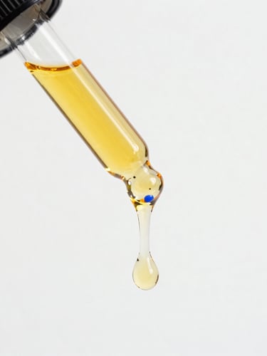 Macro close-up of golden cold-pressed botanical oil dripping from a minimalist glass dropper, bright high-key daylight, clean white background, 35mm lens