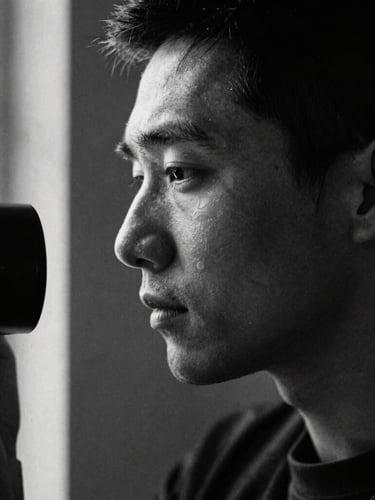 Close-up portrait of a cinematic photographer in profile, soft window light highlighting the face, grainy black and white film texture, deep dark shadows, high contrast chiaroscuro composition.