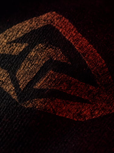 Macro crop of thick black cotton fabric texture, showing the high-density screen print of a gold graphic, dramatic low-key lighting, deep shadows, gritty 35mm grain.