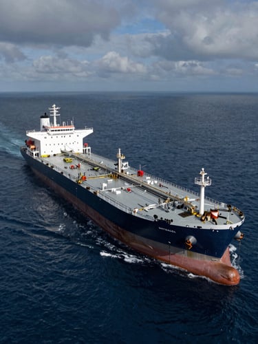 Aerial view of a large crude oil tanker at sea, deep steel blues and grays, overcast sky, dramatic high-contrast lighting
