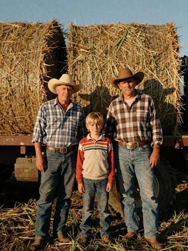 An unposed portrait of the Seely family standing by a flatbed truck loaded with freshly baled alfalfa, warm low-angle afternoon sun, authentic agrarian attire, 35mm film