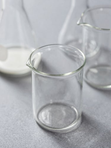 Macro photograph of clean laboratory glassware under bright daylight, soft shadows, slate-gray background, shallow depth of field.