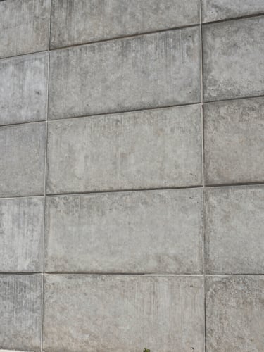 Low-angle architectural shot of a massive concrete retaining wall, uniform gray tone, industrial aesthetic, high-contrast daylight