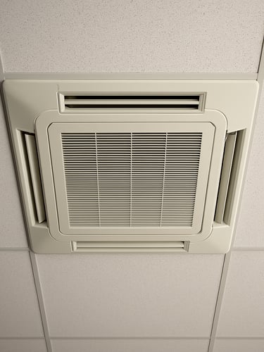 Overhead technical view looking up at a cassette air conditioning unit flush-mounted in a suspended drop ceiling tile grid, white diffuser grille visible centered in the ceiling panel, neutral office lighting, sharp focus on the unit edges and ceiling grid lines, no people