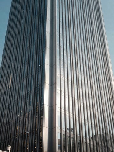 Low-angle architectural shot of a modern corporate tower in Mong Kok, Kowloon, sharp geometric shadows, cool brushed silver facade, crisp daylight.