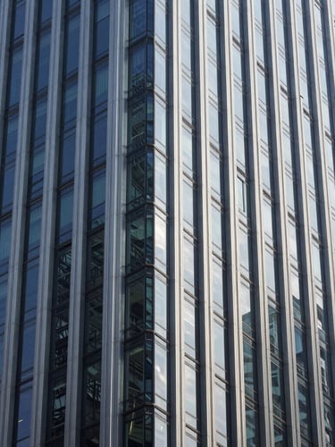 Sharp architectural close-up of a modern corporate skyscraper facade in Mong Kok, steel and glass geometry, cool daylight, high-contrast shadows.