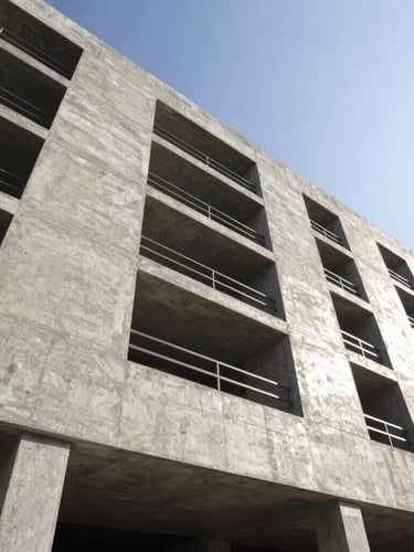 Low-angle architectural photography of a modern concrete building facade under construction in Lima, sharp morning sun casting clean geometric shadows, high-contrast steel and concrete, professional.
