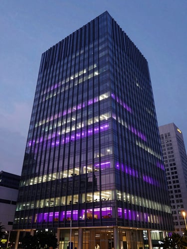 Structured wide angle of a modern Jakarta financial district office building at dusk, cool ambient twilight, subtle purple and magenta interior lighting visible through glass windows, 35mm lens.
