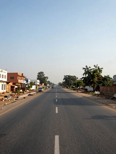 Wide environmental shot of a paved two-lane district road in Jhajjar, Haryana under natural afternoon light, low-rise commercial buildings visible on the left side, open sky above, no people in frame, shot from road level showing depth and spatial scale