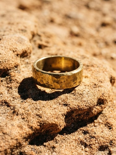 Macro shot of a heavy hand-hammered brass ring resting on textured sandstone under harsh, direct desert sunlight with sharp, dramatic shadows