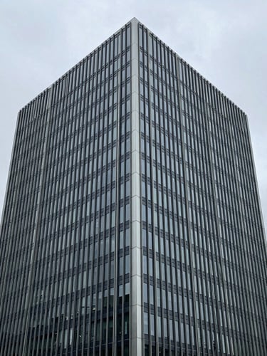 Architectural steel-and-glass crop of a modern European financial headquarters, overcast daylight, desaturated navy tones, 35mm