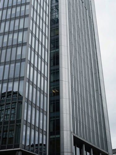 Low-angle architectural crop of a modern European financial headquarters in Frankfurt, steel and glass facade reflecting cool overcast daylight, desaturated navy and platinum tones, minimalist composition, 35mm.