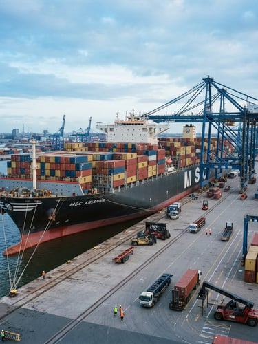 Wide environmental shot of a massive container vessel docked at a modern deepwater port, cool daylight, metallic grays and deep blues, sharp focus, 35mm