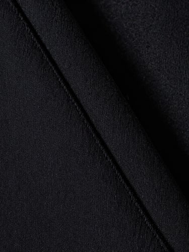 Extreme macro close-up of heavy black cotton fabric weave, showing sharp architectural seam detail, stark high-key studio lighting, desaturated monochromatic tones.