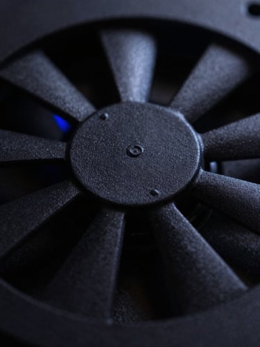Macro close-up of a matte black 3D printed fan grill with low-key single-source lighting and a subtle blue ambient glow.