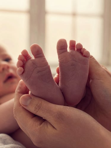 Close-up of tiny newborn baby feet held gently in mother's hands, warm golden light, emotional premium portrait