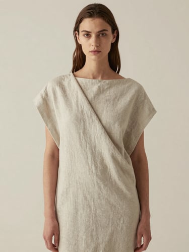 Portrait of a model wearing a monolithic draped dress in raw linen, soft diffused north-facing daylight, minimalist cream background.