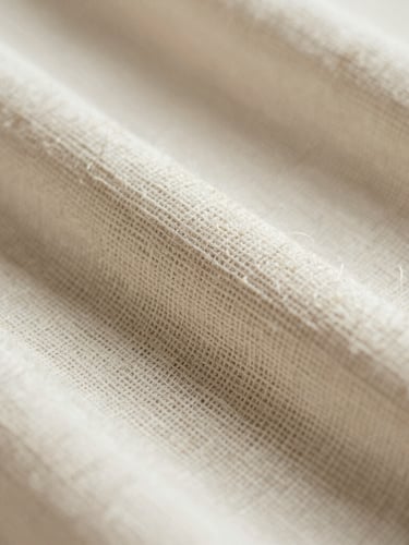 Macro close-up of hand-woven organic cotton fabric, showing the intricate raw texture and individual threads under soft directional daylight.