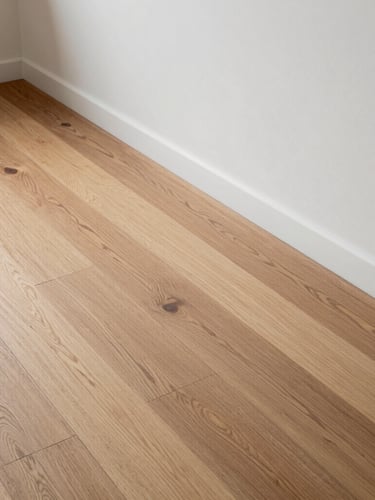 High-angle architectural elevation of historic wide-plank oak floorboards transitioning precisely to a clean plaster wall, showcasing natural wood grain and tight tolerances under cool daylight.