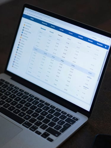 Close-up overhead view of a laptop screen displaying a multi-currency transaction dashboard with payment routes, currency codes, and settlement status rows, cool blue monitor glow on a dark desk surface, no human faces