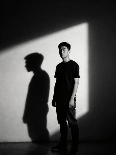 A dramatic portrait of a photographer in a minimalist studio, sharp chiaroscuro lighting, deep shadows, high contrast black and white, 35mm film grain