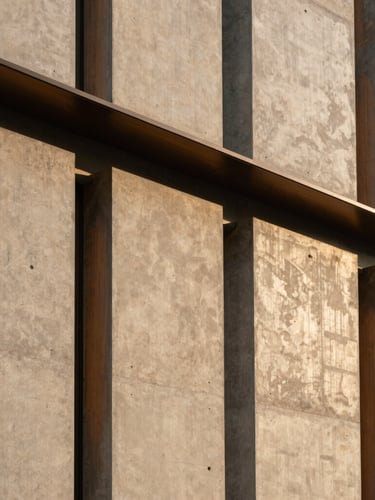 Detail of a contemporary commercial building facade, concrete panels and brushed bronze accents, geometric structural lines, afternoon light, 35mm lens.