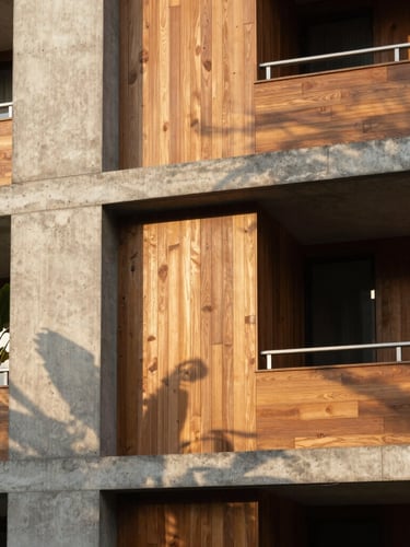 Vertical architectural shot of a brutalist concrete facade integrated with warm wood paneling, tropical vegetation casting soft shadows, afternoon sun, 35mm lens.
