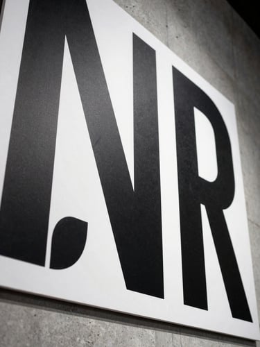 Extreme close-up of a large-format environmental graphic panel mounted on raw concrete, stark studio strobe lighting revealing texture and ink density, a single bold typographic treatment visible in high contrast black on white, shot tight from below at a slight upward angle