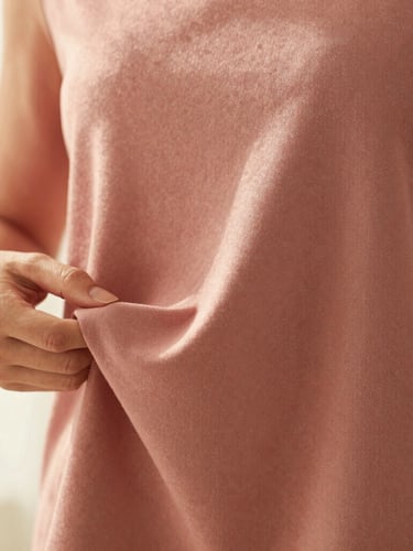 Close-up fabric texture detail of a dusty rose modest blouse, hands gently holding the soft drape of the fabric, warm morning light, 35mm