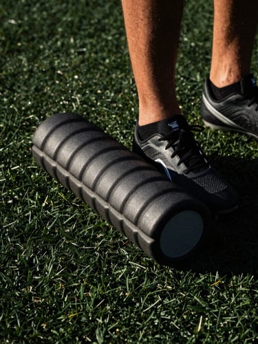 Tight crop on a foam roller and cleats on dark gym turf, harsh dramatic lighting, high contrast.