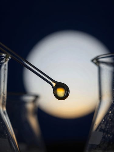 Macro high-contrast photograph of laboratory glassware containing a glowing amber chemical formulation, deep navy background, cool-toned scientific backlighting, sharp focus on molecular droplets, planetary sunrise-gold accents on the horizon of the glass curves.
