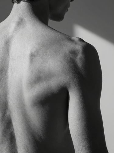 Close-up studio study of a male back, shoulder blade and spine rendered in precise chiaroscuro, strobe light from the upper right casting a hard diagonal shadow, black and white, skin texture as formal subject, no romanticism