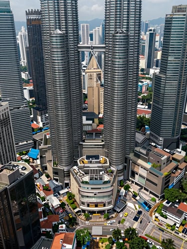 Wide overhead urban map perspective of Kuala Lumpur city district, clean daylight, dense mid-rise and high-rise blocks forming structured street grid, arterial roads and transit lines visible, no labels or text overlays, architectural precision framing