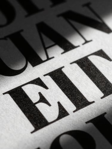 Extreme close-up of a high-contrast typographic layout on textured paper, dramatic side light with harsh shadows, sculptural composition, editorial studio photography style