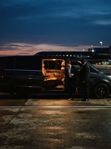 Sleek dark private transport van waiting on a runway at dusk, warm interior light, modern editorial travel photography, 35mm