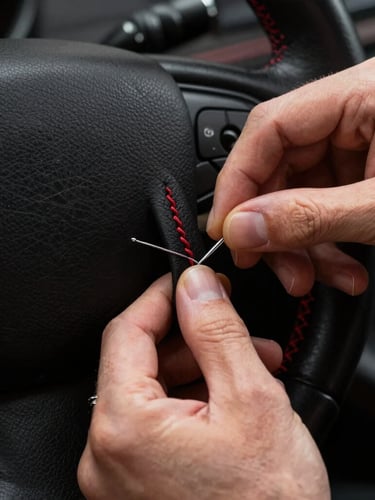 Extreme close-up of artisan hands stitching black Nappa leather onto a steering wheel, red double-stitch detail, dramatic workshop key lighting, dark background