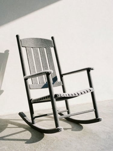 A matte charcoal resin rocking chair on a minimalist plaster porch, covered in light winter frost, sharp morning shadows, crisp architectural photography.