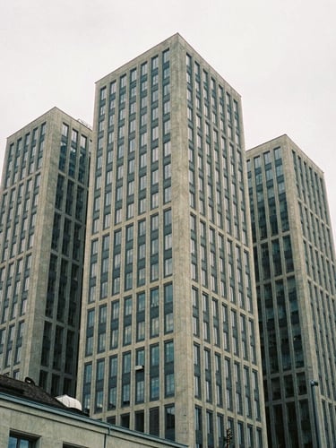 Architectural crop of a Zurich financial hub, sharp concrete lines against soft overcast daylight, desaturated navy and sand tones, 35mm film grain